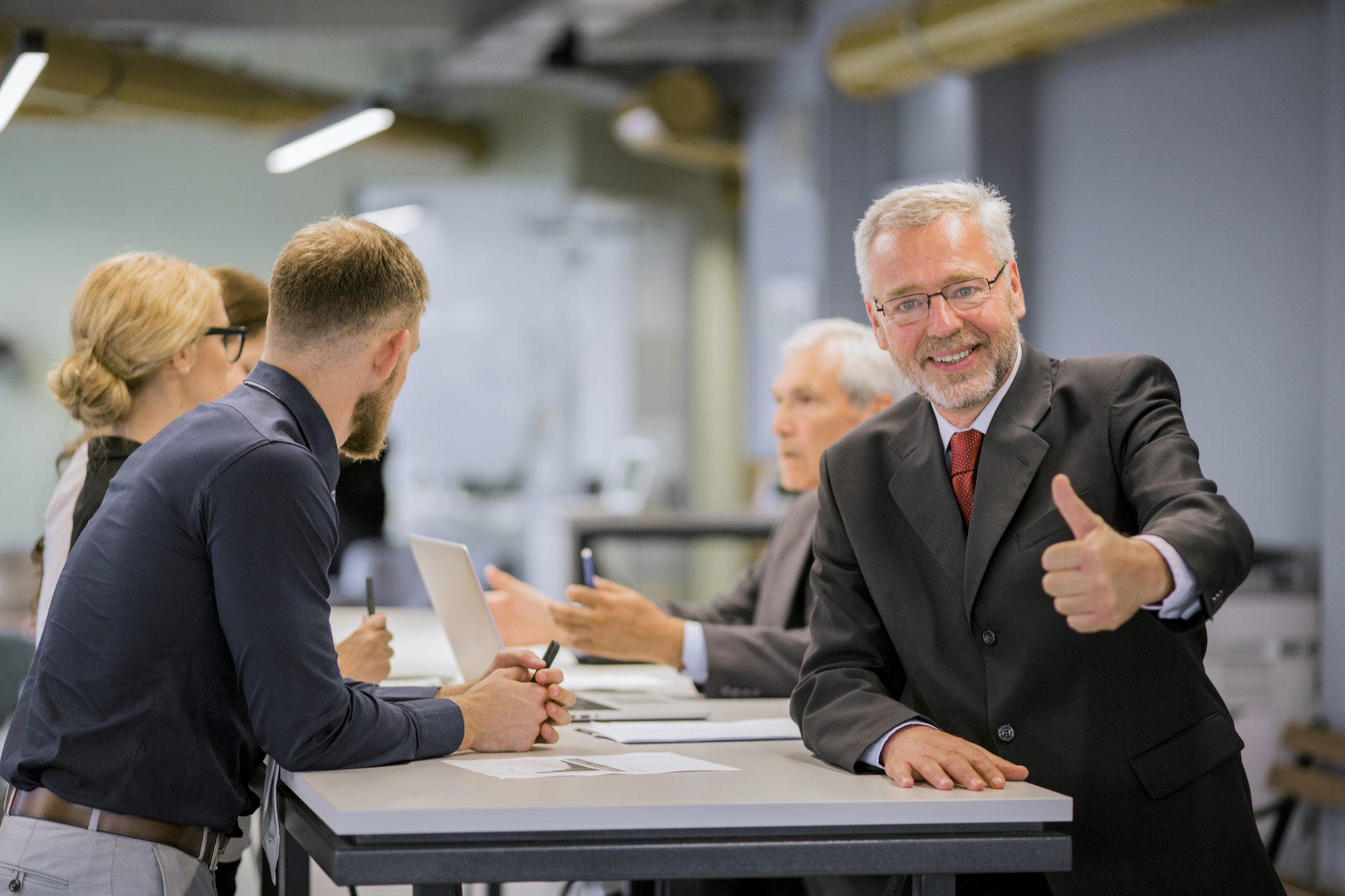 Homme en costume fait le signe du pouce levé.